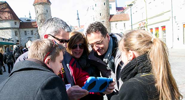 Group of men and women looking to the screen of an iPad in the old town of Tallinn.