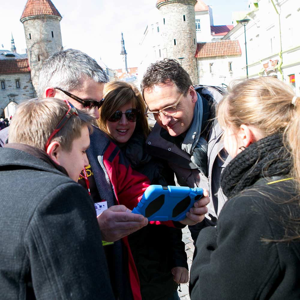 Group of men and women looking to the screen of an iPad in the old town of Tallinn.